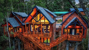 Eine hölzerne Blockhütte mit mehreren Ebenen, die durch Holztreppen verbunden sind, inmitten eines bewaldeten Gebiets.