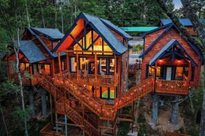 Eine hölzerne Blockhütte mit mehreren Ebenen, die durch Holztreppen verbunden sind, inmitten eines bewaldeten Gebiets.