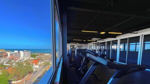Une salle de sport équipée de matériel d’exercice et offrant une vue sur le paysage urbain de la côte.
