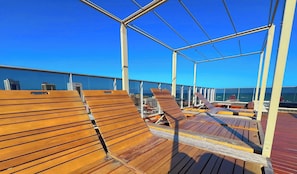 A deck with wooden seating and a glass railing, overlooking a cityscape. - Villi Desing - Miramar Hospedagens  (João Pessoa)
