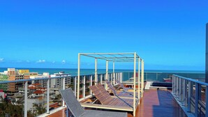 Une terrasse sur le toit avec des chaises longues, une pergola en métal et une vue sur l’océan.