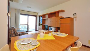 A dining area with a wooden table set for two, a microwave, and a refrigerator in the background. - Apartment Overlooking the sea and the Marina (Lignano Sabbiadoro)