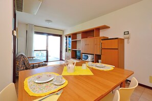 Ein Essbereich mit einem Holztisch, gedeckt für zwei Personen, sowie einer Mikrowelle und einem Kühlschrank im Hintergrund.