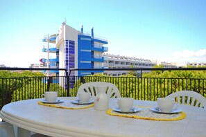 Ein Balkon mit Tisch für zwei Personen, weißen Stühlen und einer weißen Karaffe. Im Hintergrund ein blau und weiß gestrichenes Gebäude.