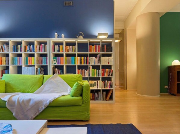 Une pièce avec un canapé vert, une bibliothèque remplie de livres et un plancher en bois.