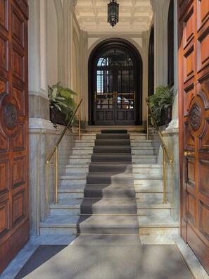 Une entrée imposante avec des marches en marbre, des portes richement décorées et une lanterne classique.