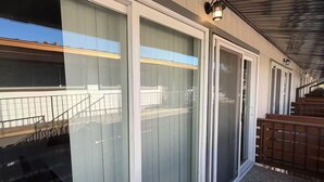 En byggnad med stora skjutbara glasdörrar, en täckt uteplats med ett trädäck och ett metallräcke.