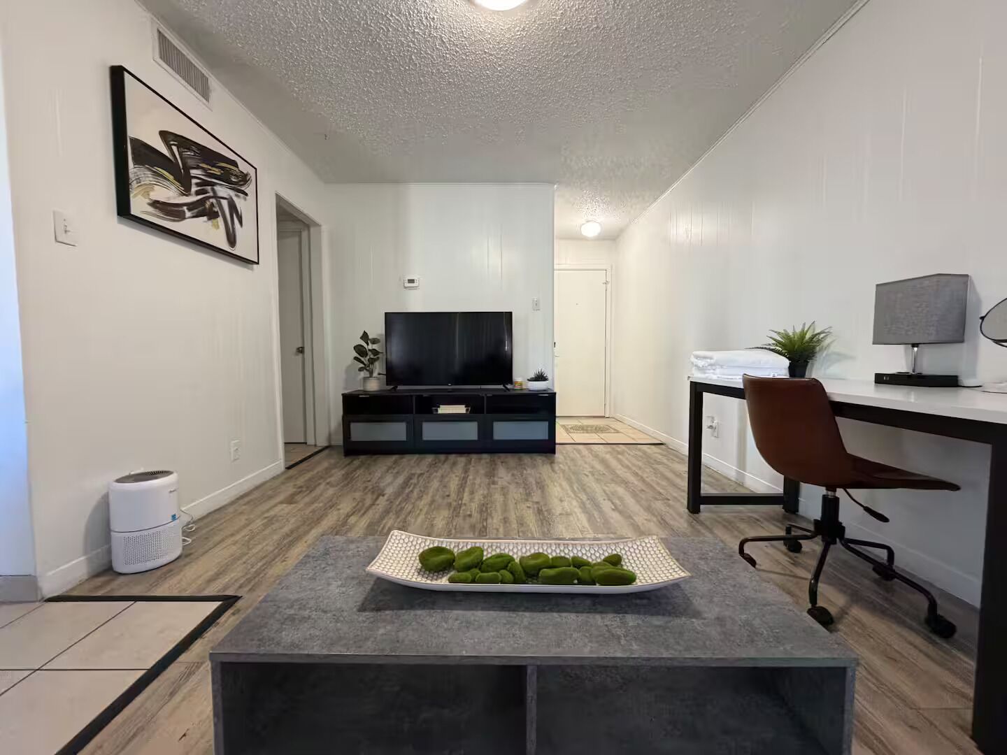 En moderne stue med et fladskærms-tv, et spiseområde med et bord og en stol, samt en lille plante på skrivebordet.
