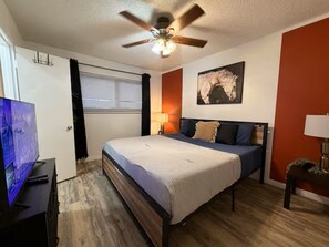 Ein Schlafzimmer mit Bett, Deckenventilator, Kunstwerken und einem Fernseher.