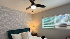Ein ordentlich bezogenes Bett mit weißen Leinen, einem türkisblauen Kopfteil und einem Deckenventilator.