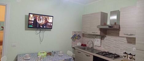 A compact kitchen with a dining area, a TV mounted on the wall, and a modern light fixture.