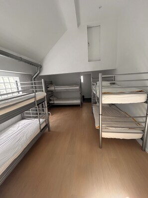 Ein Schlafsaalzimmer mit Stockbetten, Holzboden und einem kleinen Fenster.