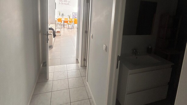 A hallway leading to a bathroom with a bathtub and a dining area in the background. - Lemon Apartment (Schaerbeek)