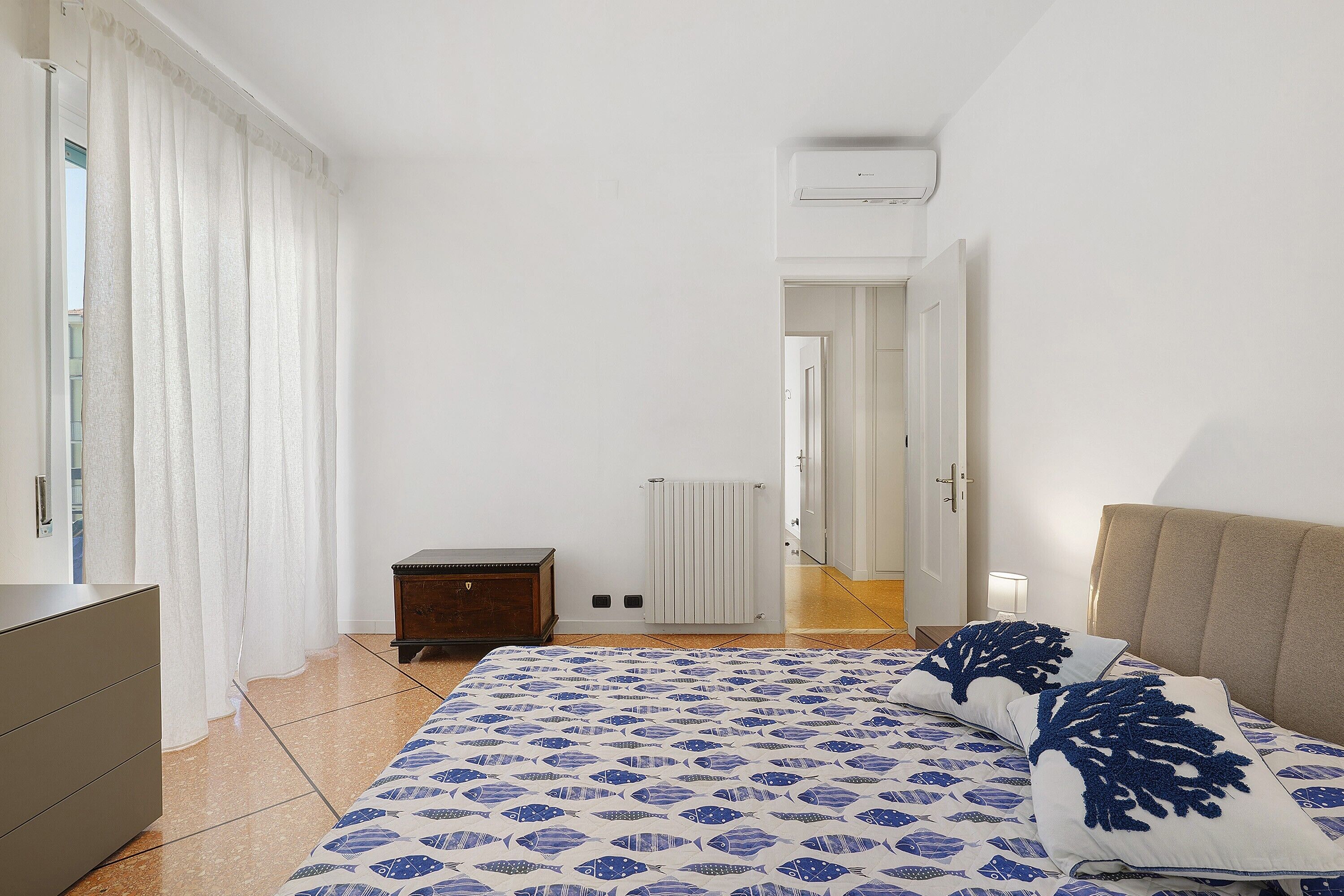 Une chambre à coucher comprenant un lit, une commode, un radiateur et une porte donnant sur une autre pièce.