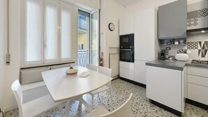 A kitchen with a white table, chairs, a microwave, oven, and a clock on the wall. - Apartment 'Beautifulliguria' with Balcony, Wi-Fi and Air Conditioning (Sestri Levante)