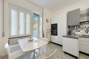 Eine Küche mit einem weißen Tisch, Stühlen, einer Mikrowelle, einem Backofen und einer Uhr an der Wand.