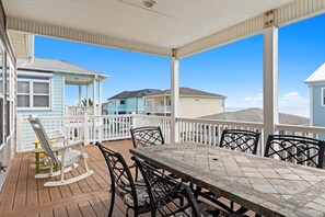 Eine überdachte Terrasse im Freien mit Tisch und Stühlen, einer Schaukel und Blick auf benachbarte Häuser.