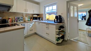 Cozinha moderna com armários brancos, micro-ondas, cafeteira e janela com vista para uma cerca de madeira.