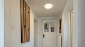 Um corredor com um banco, um tapete estampado, uma porta com espelho e uma luminária no teto.