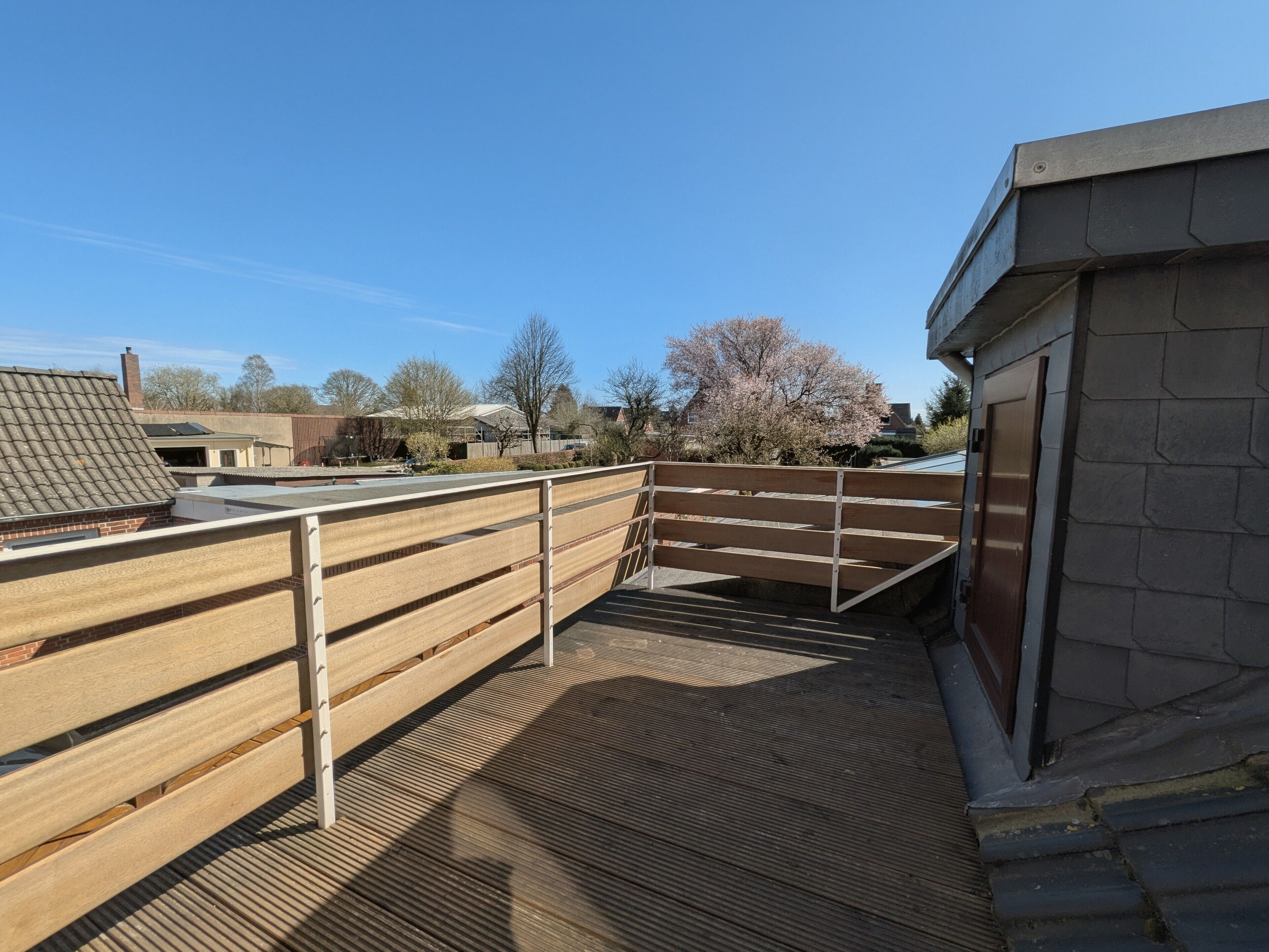 A rooftop terrace with a wooden fence, a ramp leading to a building entrance, and a clear blue sky.