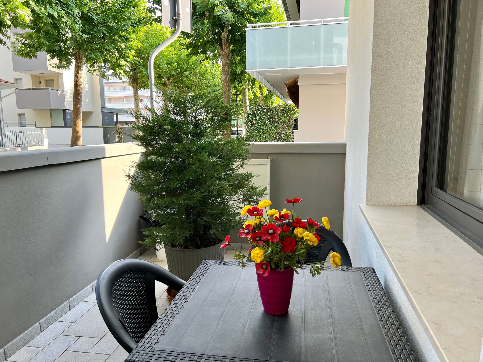 A balcony with a table, chairs, a potted plant, and a flower arrangement.