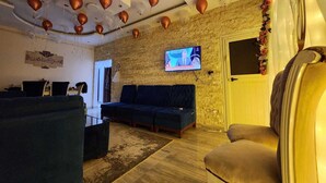 Een woonkamer met een bakstenen muur, een aan de muur bevestigde televisie, een bank, een fauteuil en een plafond met decoratieve details.