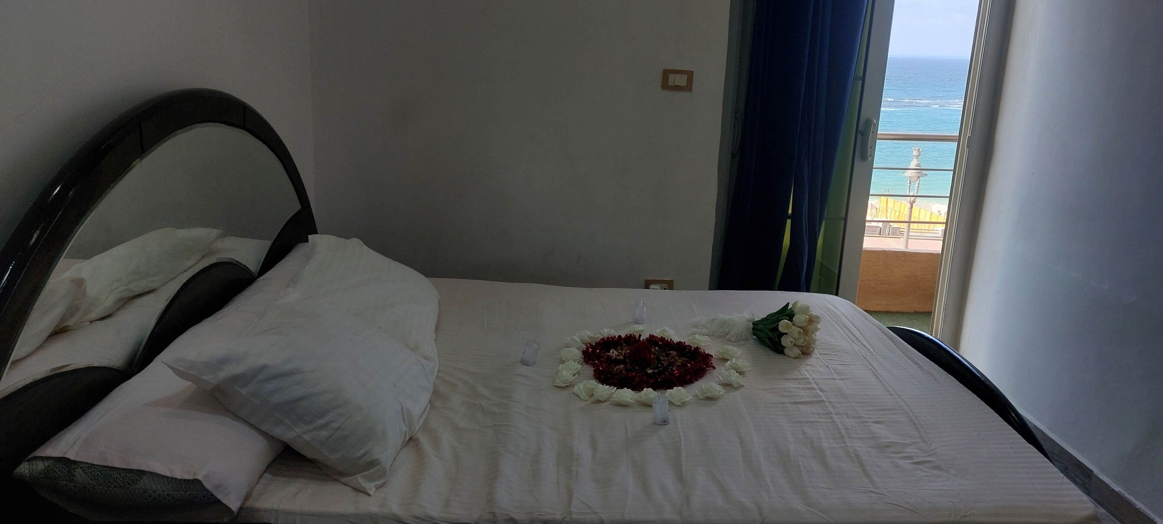 A bed with white linens, a dark headboard, and a bouquet of flowers on the bed.