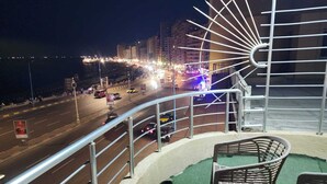 Een balkon met uitzicht op een drukke straat 's nachts, met metalen hekwerk en twee stoelen.