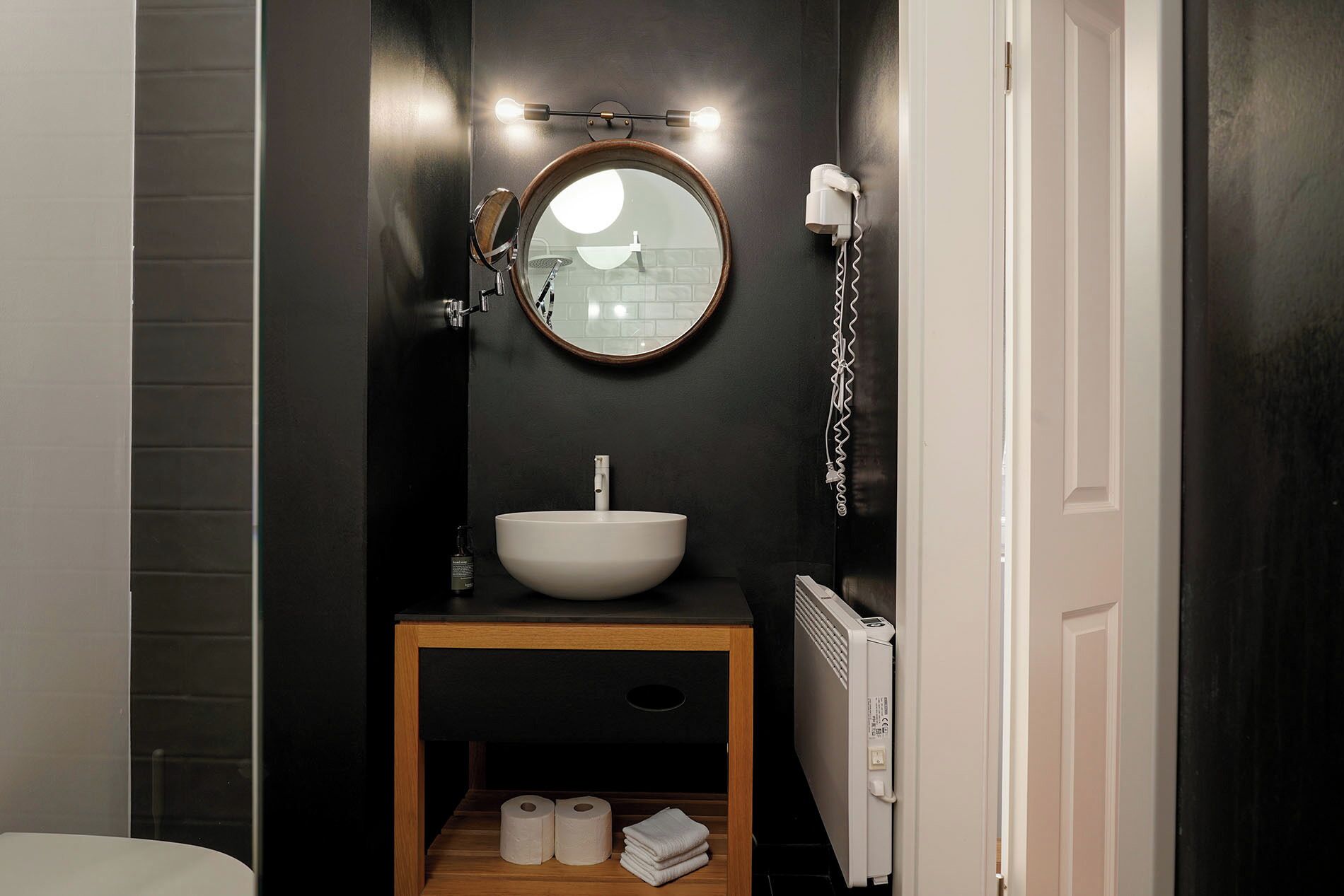 A bathroom with a round mirror, a white sink, and a wooden vanity.