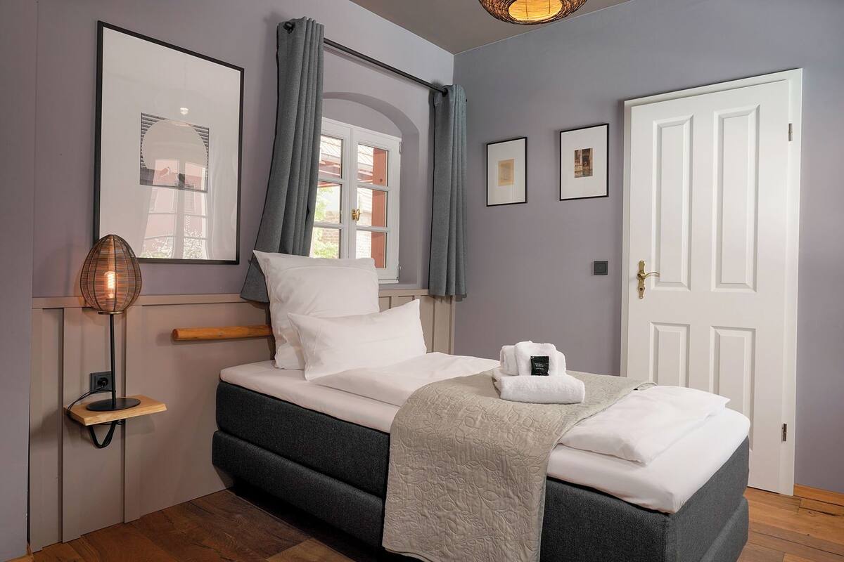 A neatly arranged bedroom with a bed, a bedside lamp, a door, and framed pictures on the wall.