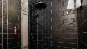 A shower with a black rain shower head, a handheld showerhead, and a bottle of shampoo on the wall. - Wohnkultur DSIGNIO Digital Hotel (Ladenburg)