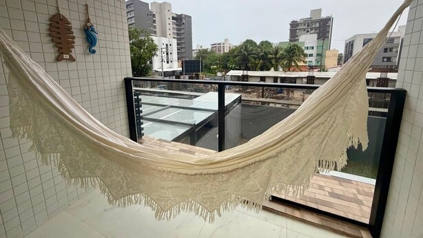 Une pièce avec un hamac, un mur recouvert de carreaux et une vue sur des immeubles.