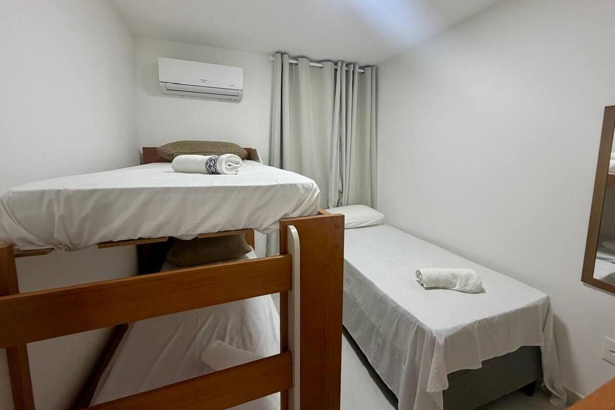 Een kleine, schone kamer met een stapelbed, een enkel bed, een spiegel en een airconditioning.