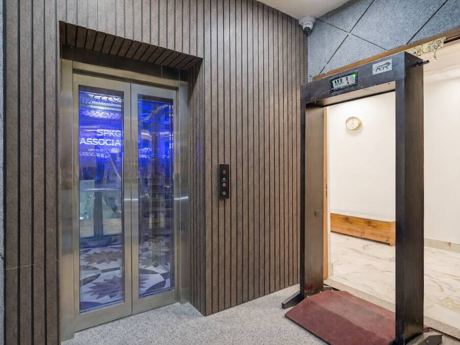 Un ascensor con pantalla digital, revestimiento de pared de madera y puerta de vidrio con reflejos.