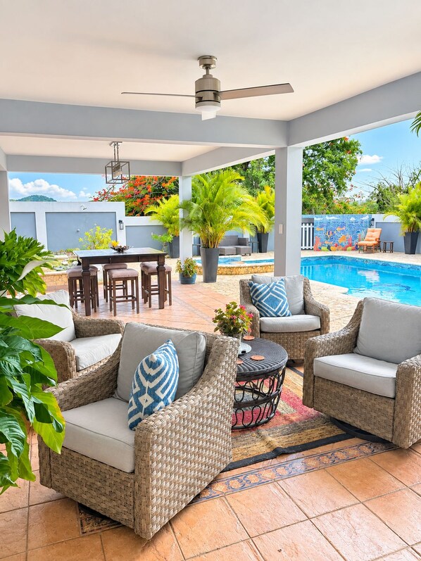An outdoor patio area with wicker furniture, a pool, and a ceiling fan.