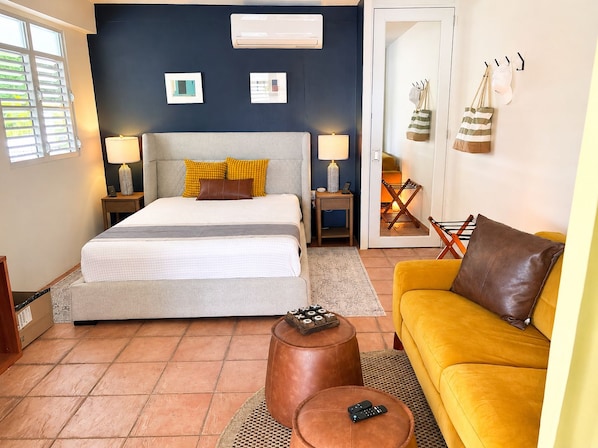 A bedroom with a bed, bedside lamps, a sofa, a coffee table, and a door leading to a balcony.