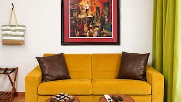 A yellow sofa with two brown cushions, a framed artwork above, and a green curtain to the right.