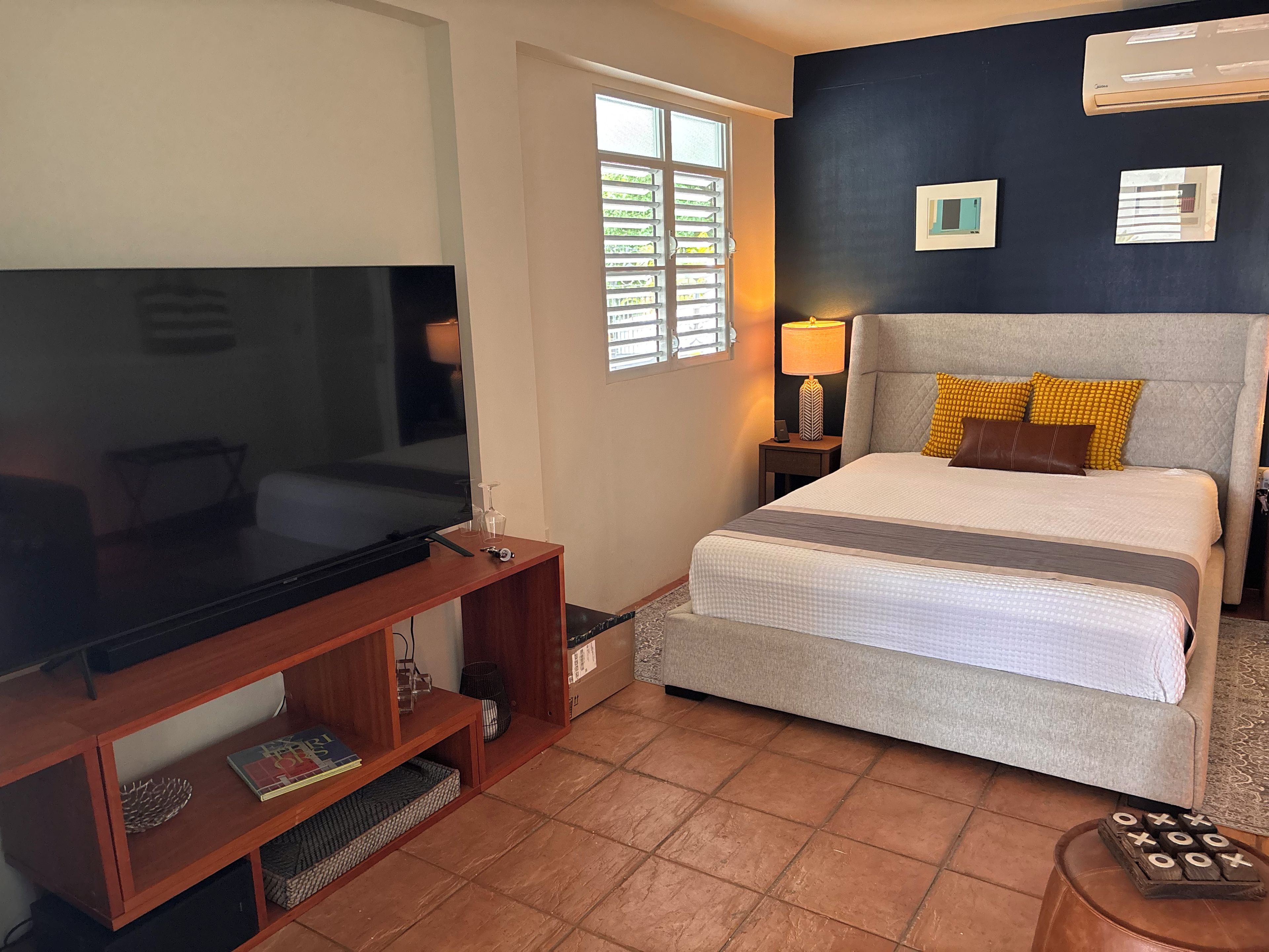 Une chambre d’hôtel équipée d’une télévision, d’un lit, d’une table de chevet avec une lampe et d’une fenêtre avec des stores.