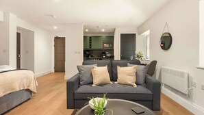 A modern living room with a sofa, a coffee table, and a kitchen in the background. - Contemporary Spacious Studio in Central Sheffield (Sheffield)