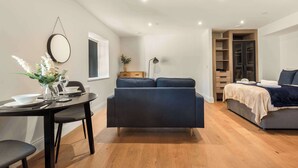 A modern living room with a sofa, a dining table with chairs, a small side table with a vase and wine glasses, a mirror on the wall, and a bed with a blue blanket. - Contemporary Spacious Studio in Central Sheffield (Sheffield)