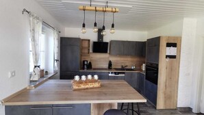 A modern kitchen with a wooden island, dark cabinets, and pendant lighting.