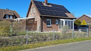 A residential house with a solar panel roof, a fenced yard, and a clear blue sky.