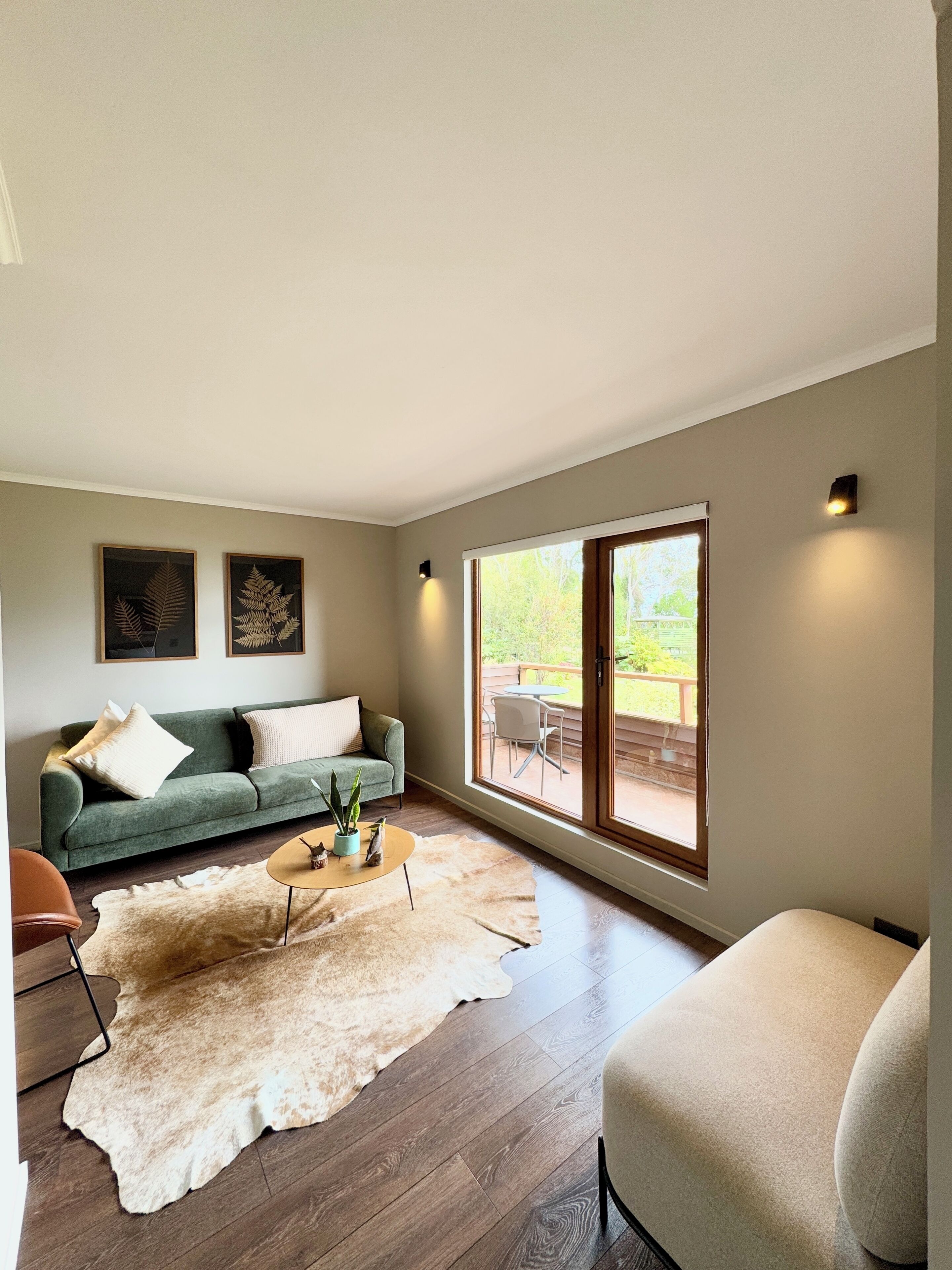 A modern living room with a green sofa, a white rug, and a large window with a view of the outdoors.