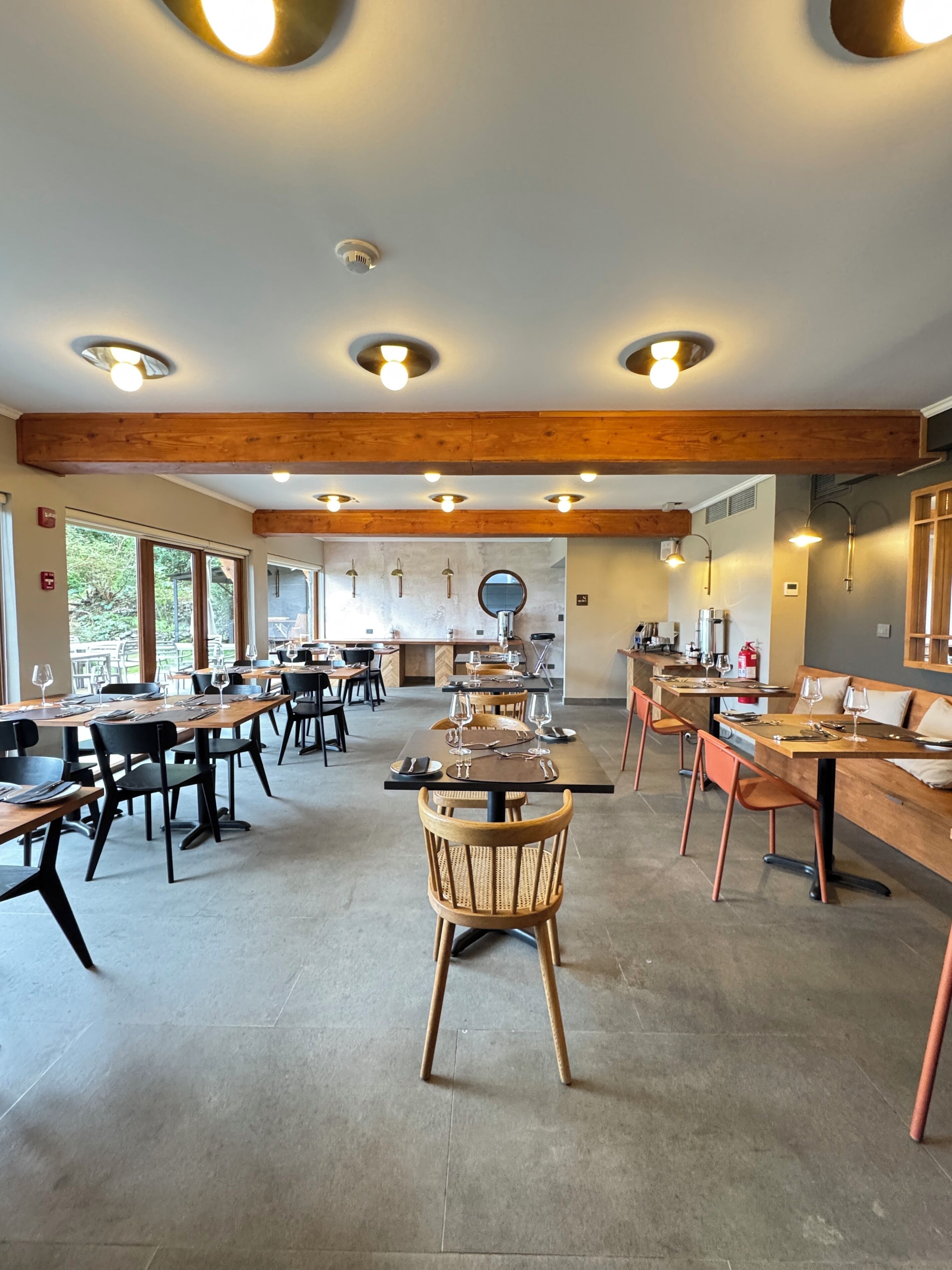 Un comedor amplio con mesas y sillas de madera, luces empotradas en el techo y ventanas grandes.
