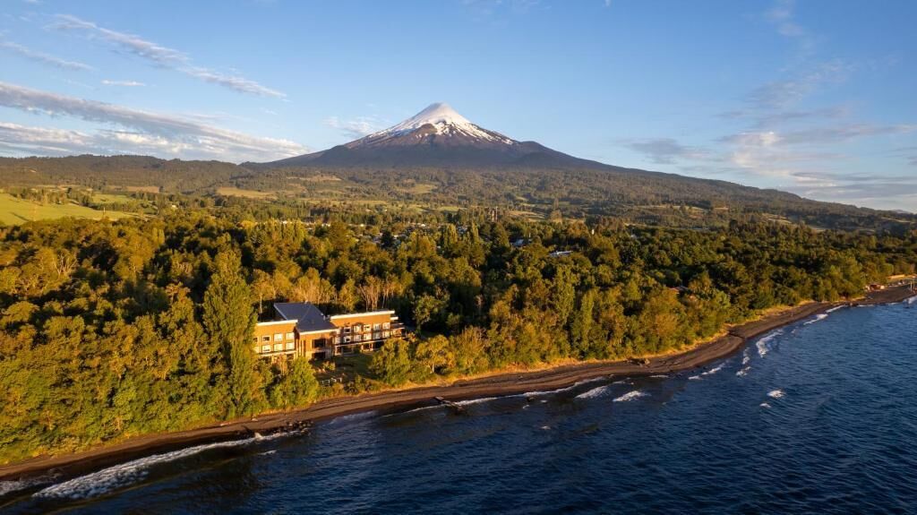 A coastal view with a mountain in the background, a beach, and a building with multiple stories.
