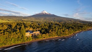Una propiedad costera con una montaña al fondo, una playa y un área boscosa.