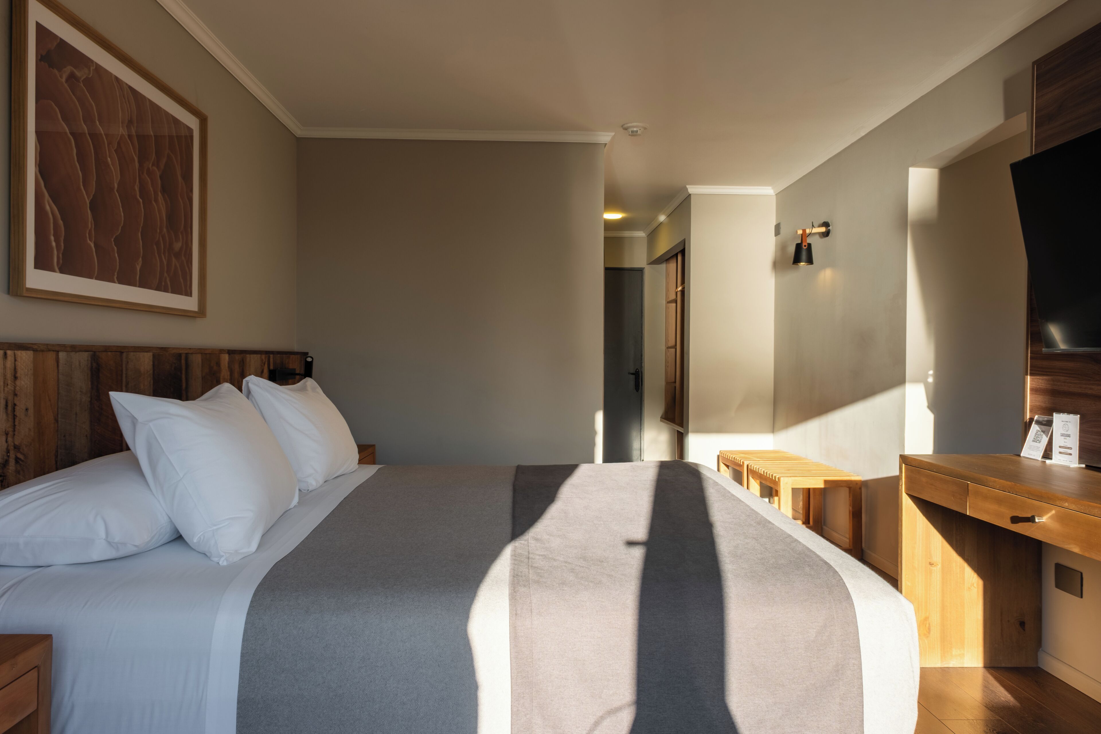 A hotel room with a large bed, a wooden headboard, a desk, a television, and a framed picture on the wall.