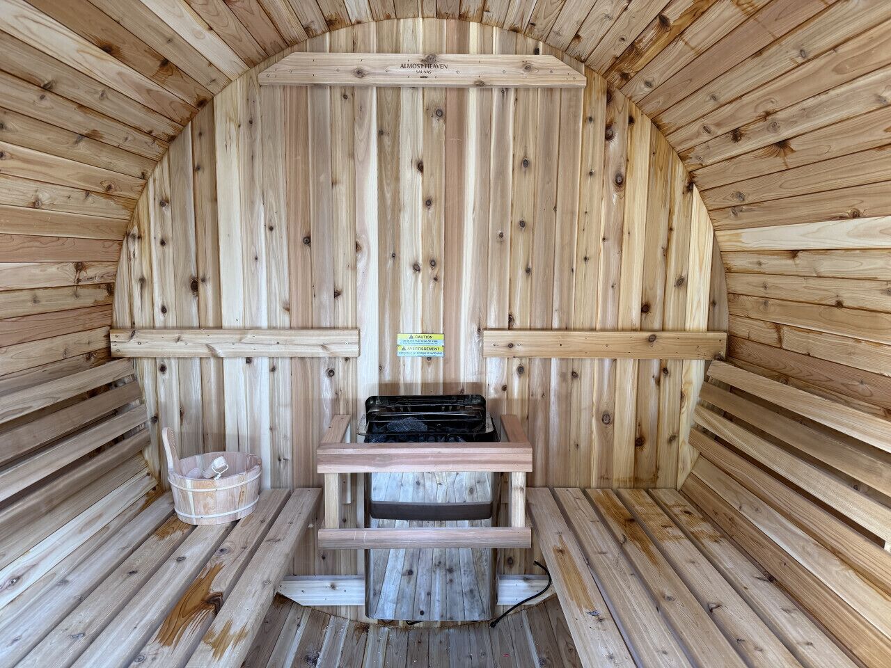 A sauna with wooden walls and benches, a bench with a towel, and a caution sign.