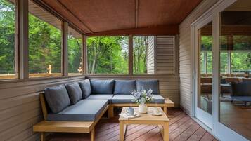 A covered porch with a sectional sofa, a wooden table, and a view of the outdoors.