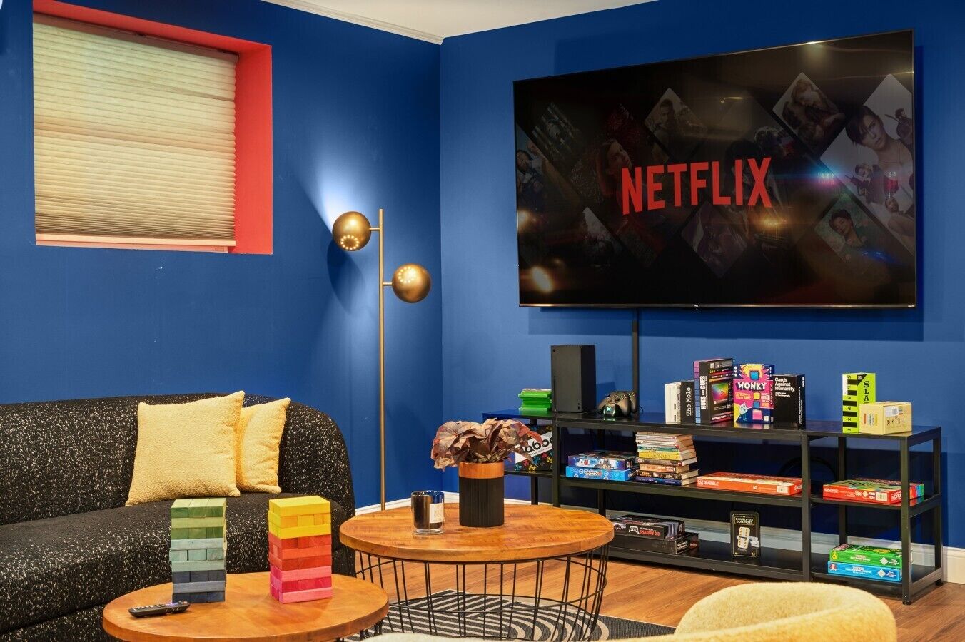 A living room with a TV displaying 'NETFLIX', a sofa, a coffee table, a bookshelf, and a floor lamp.